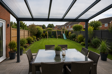 View from beneath an anthracite grey PolycarbonateX patio roof with clear multiwall polycarbonate sheets overlooking a typical British family garden.